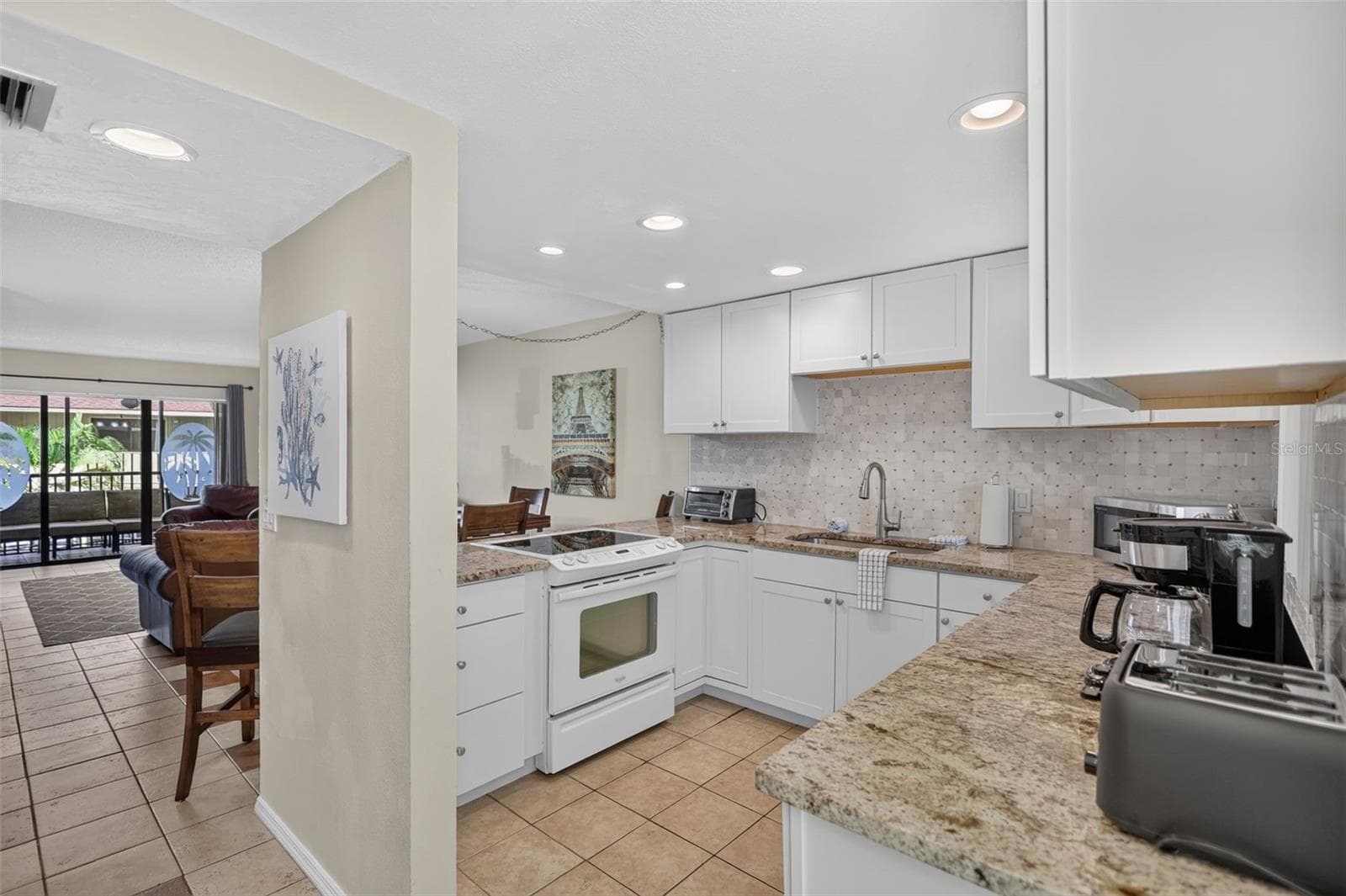 Spacious kitchen featuring granite countertops, a custom tile backsplash, and sleek modern cabinetry. - 6157 MIDNIGHT PASS RD #E53, SARASOTA
