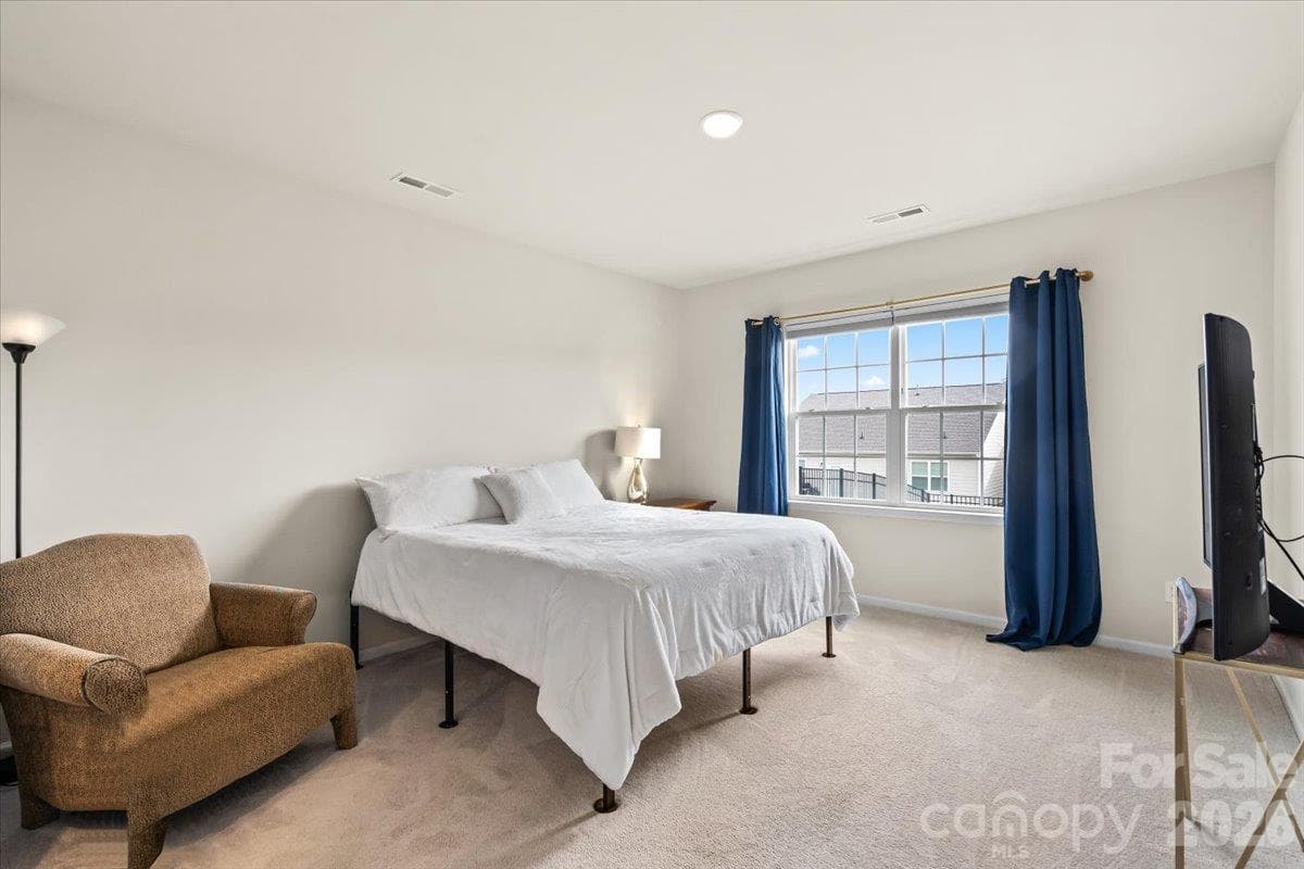 Cozy and well-lit bedroom featuring comfortable carpeting, a ceiling fan, and ample space for a small seating area. - 155 White Apple Way, Statesville