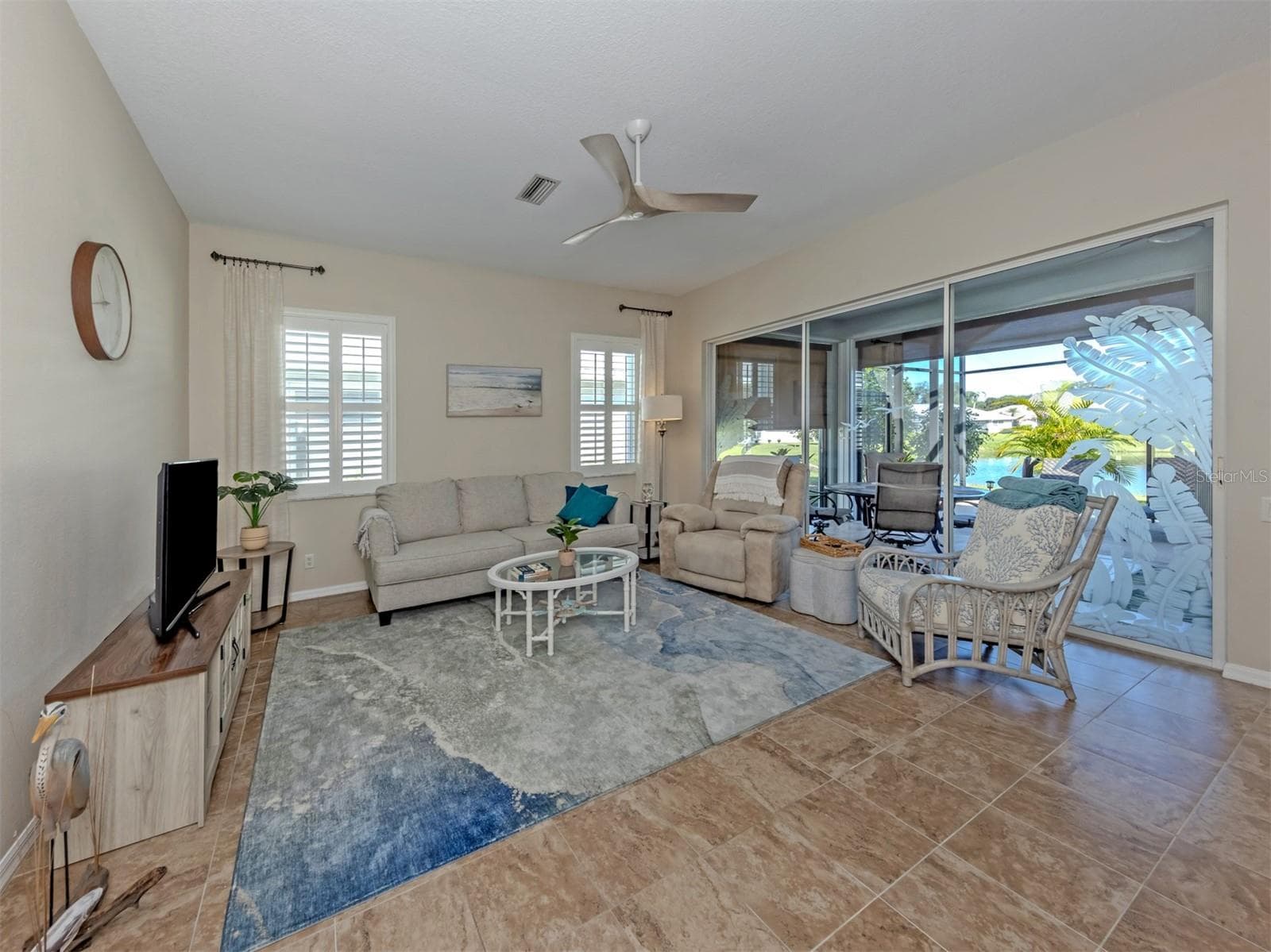 A spacious, inviting living room featuring beautiful, seamless ceramic tile flooring and elegant plantation shutters throughout the home, along with stunning etched-glass sliding doors opening to the extended lanai, bringing the beauty of the outdoors right into view! - 443 BERMUDA ISLES CIR, VENICE