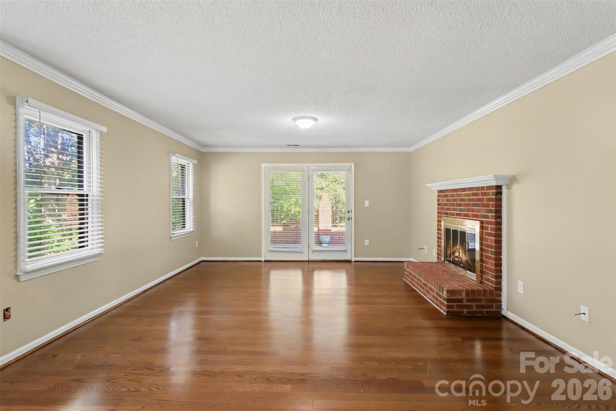 View from the dining area into the living room, featuring wood flooring, a brick gas fireplace, and glass doors opening to the rear patio. - 8407 Coulwood Oak Lane, Charlotte