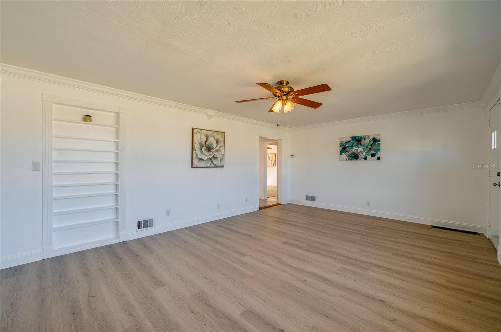Open-concept living space framed by crisp white trim, continuous LVP flooring, and a built-in recessed wall shelving unit. The clean layout and central doorway provide an airy, connected atmosphere. - 128 MINERVA RD, DAYTONA BEACH