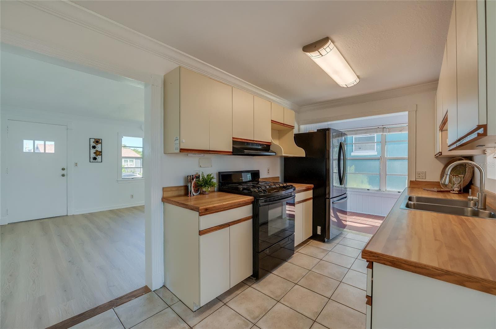 Efficient kitchen layout showcasing overhead cabinet storage, a gas range stove with range hood, and tile flooring. The open entryway offers a clear view into the adjoining bright living space. - 128 MINERVA RD, DAYTONA BEACH