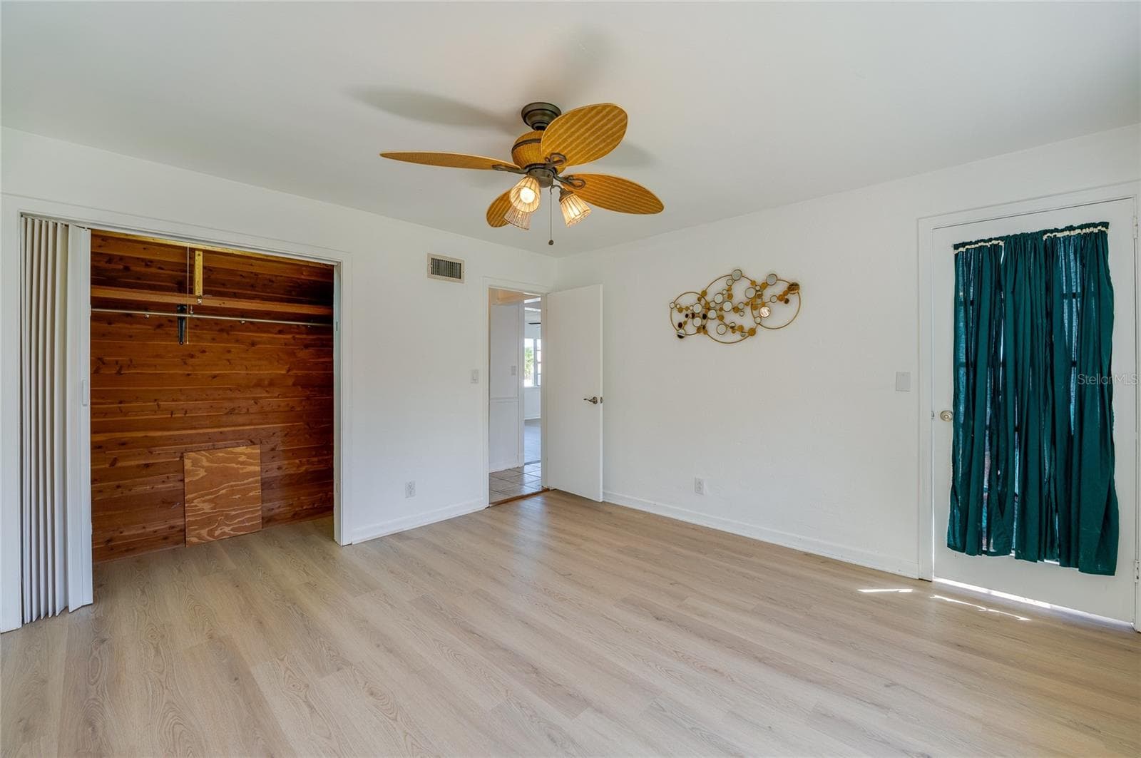 Versatile room displaying LVP flooring, a tropical-style ceiling fan, and a cedar-lined walk-in closet with built-in shelving. A glass-paneled exterior door with privacy drapery opens to an adjacent space. - 128 MINERVA RD, DAYTONA BEACH