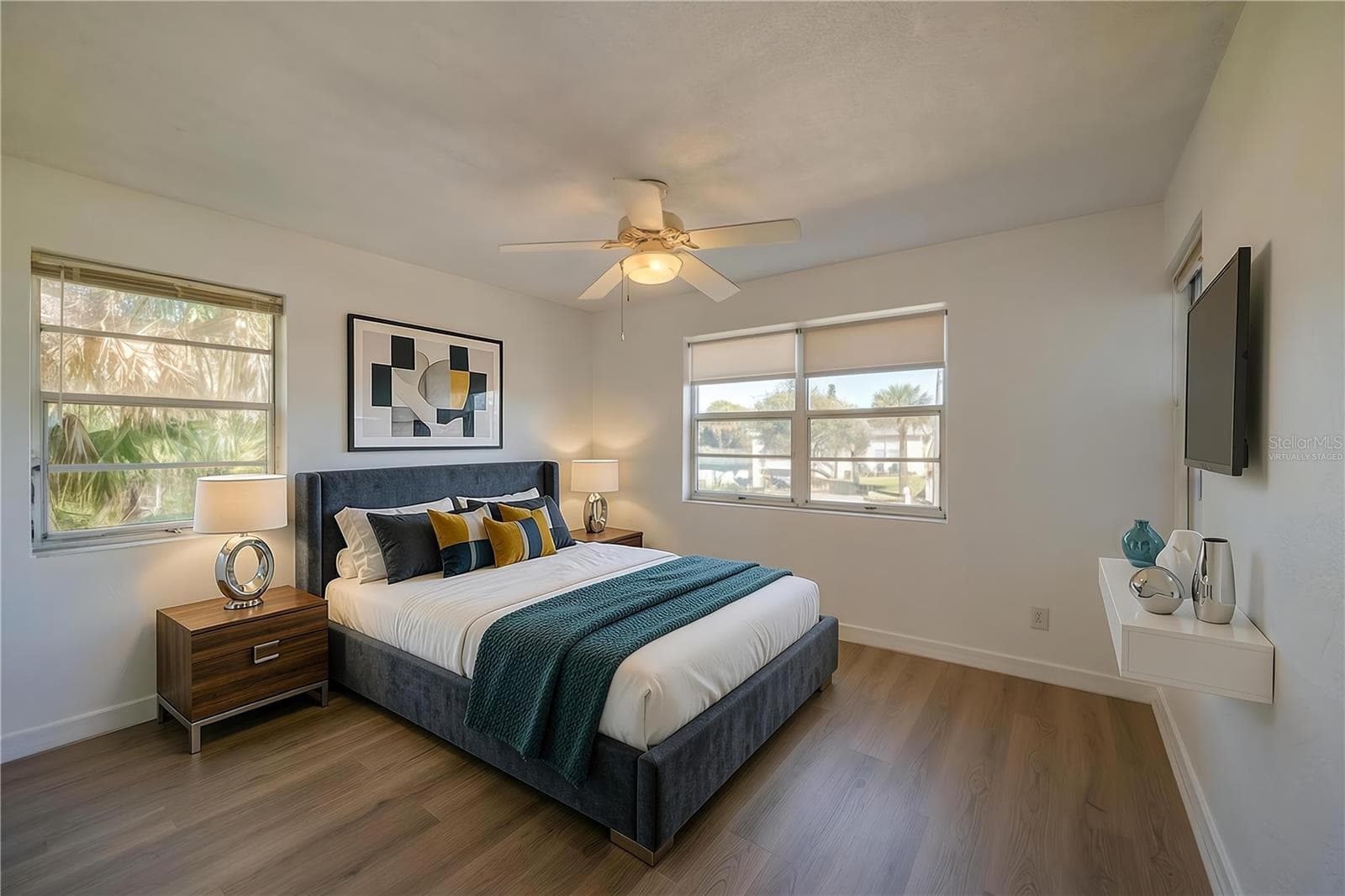 Virtually Staged - Bright bedroom area framed by continuous LVP flooring, smooth white walls, and a traditional white ceiling fan. Dual aspect windows bring in abundant sunlight and views of the surrounding palm trees. - 128 MINERVA RD, DAYTONA BEACH
