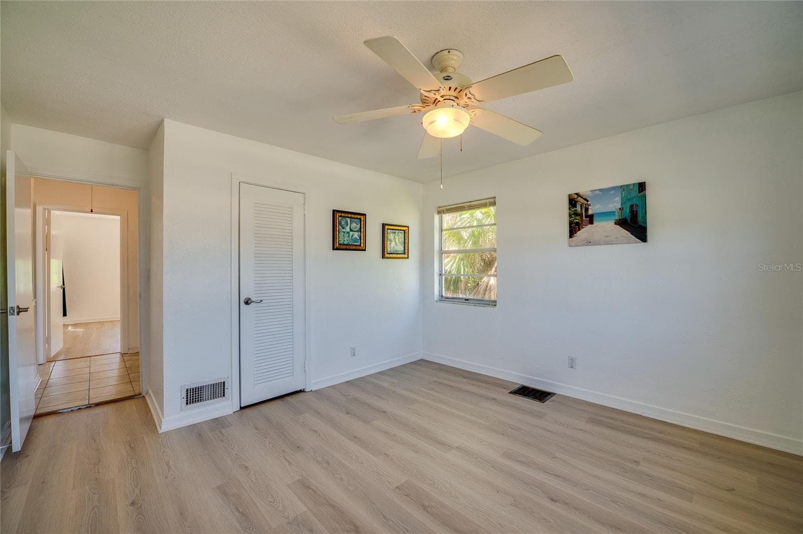 Clean interior space showcasing light flooring, a white ceiling fan, and a louvered closet door. An open doorway leads out into a tiled hallway connecting to the rest of the layout. - 128 MINERVA RD, DAYTONA BEACH