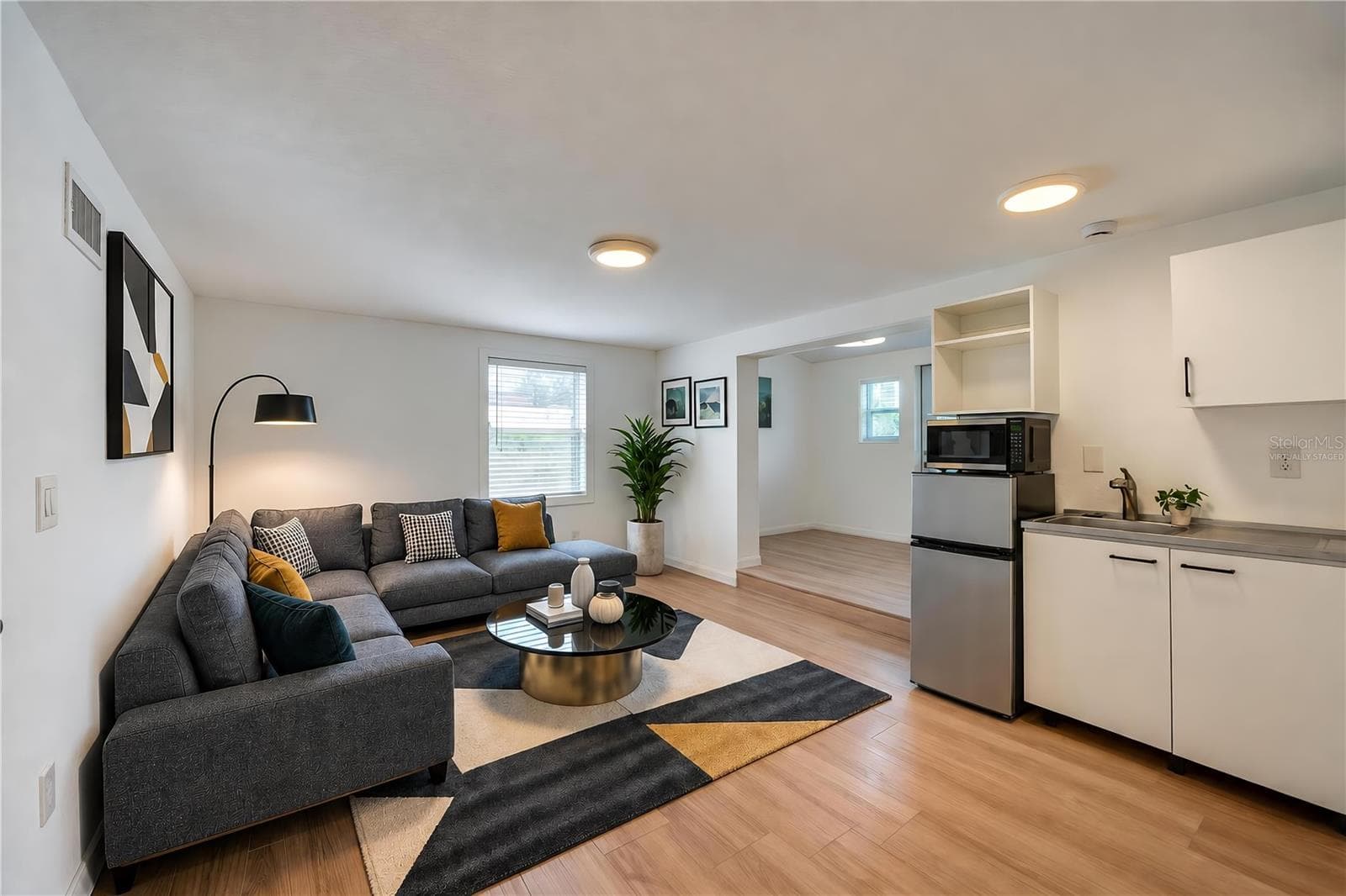 Virtually Staged - Open studio in law suite boasting modern kitchenette amenities including a compact refrigerator, microwave, sink, and low-profile cabinetry. Light LVP flooring and recessed overhead lights create a clean, contemporary feel. - 128 MINERVA RD, DAYTONA BEACH