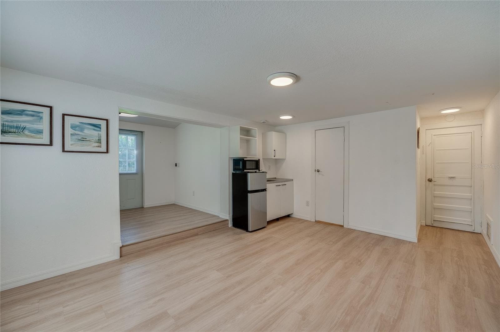 Spacious open-concept living area featuring light LVP flooring, recessed ceiling lighting, and a compact kitchenette nook. An adjacent step-up alcove provides additional versatile living space. - 128 MINERVA RD, DAYTONA BEACH