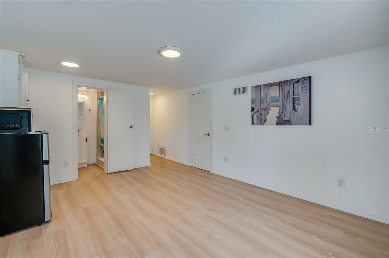 Bright indoor living space showcasing crisp white walls, LVP flooring, and recessed ceiling lights. An open doorway leads directly toward the bathroom area. - 128 MINERVA RD, DAYTONA BEACH