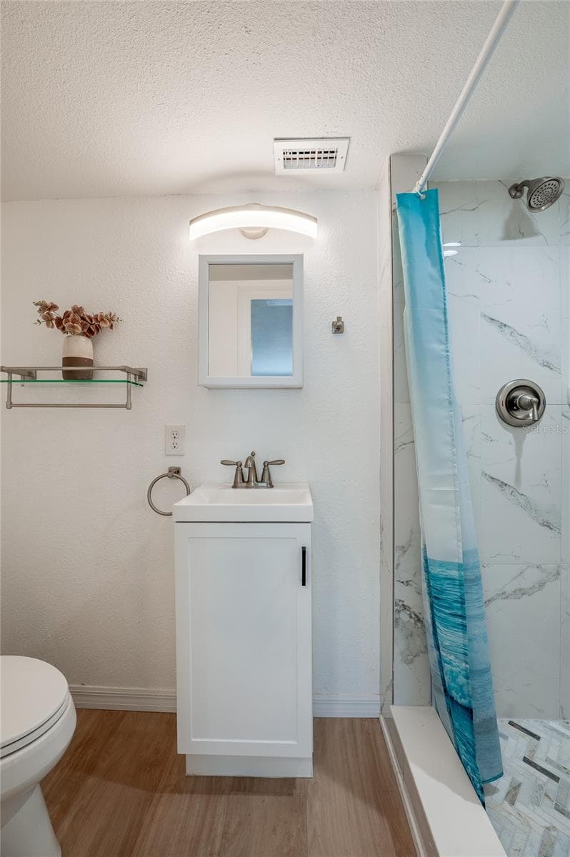 Compact bathroom area highlighting a sleek white vanity, a medicine cabinet, and bright wall sconce lighting. A walk-in shower sits alongside LVP flooring. - 128 MINERVA RD, DAYTONA BEACH