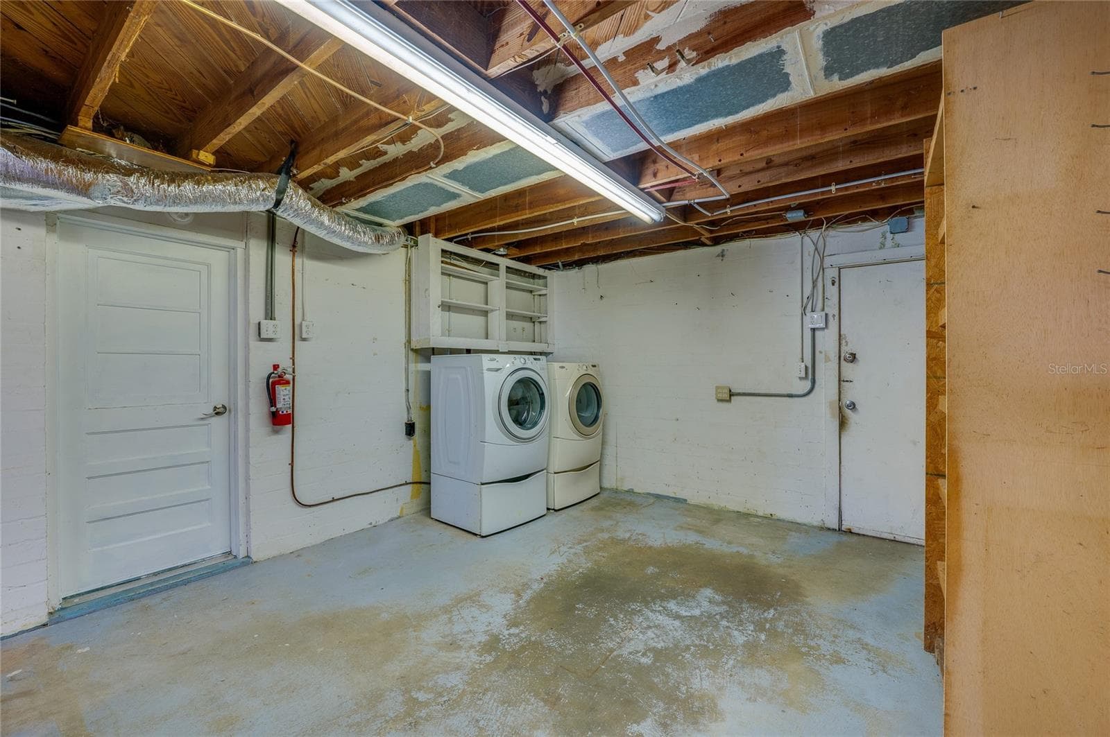 Dedicated laundry area equipped with a side-by-side washer and dryer set underneath overhead wall cabinets. The space features durable concrete floors, exposed ceiling beams, and direct door access. - 128 MINERVA RD, DAYTONA BEACH