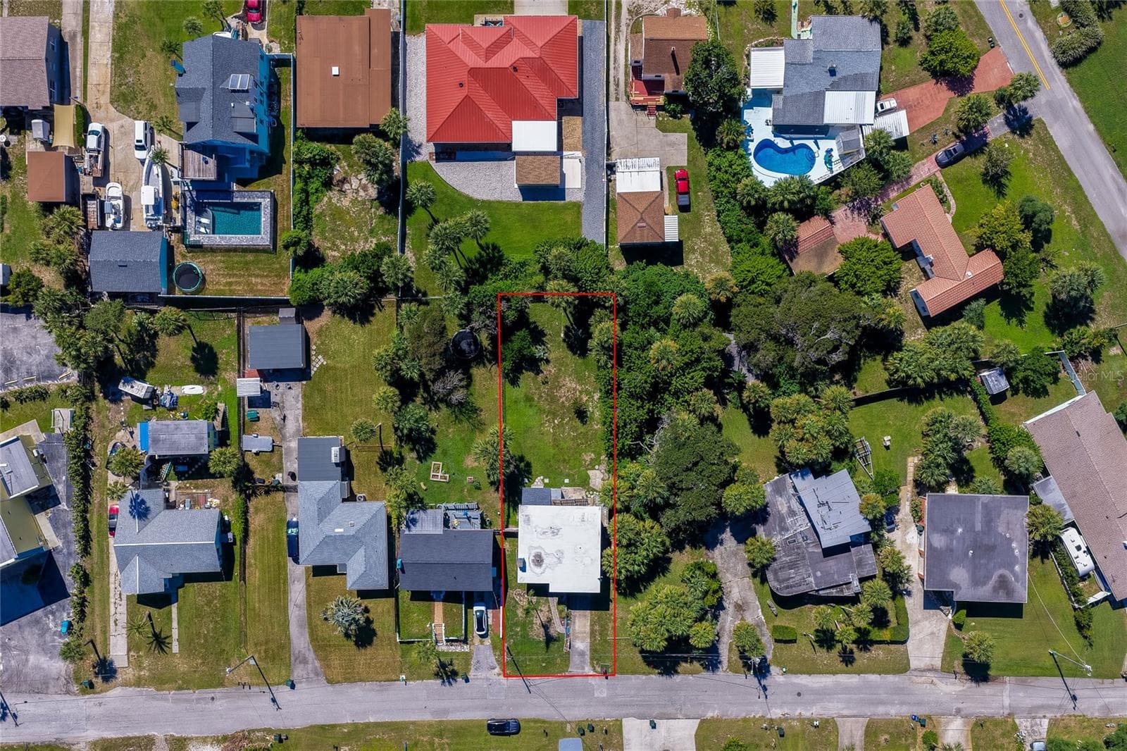 Direct overhead aerial view displaying the property boundaries outlined in red amidst a coastal residential neighborhood. Surrounding lots feature private swimming pools, lush palm trees, and detached garages. - 128 MINERVA RD, DAYTONA BEACH