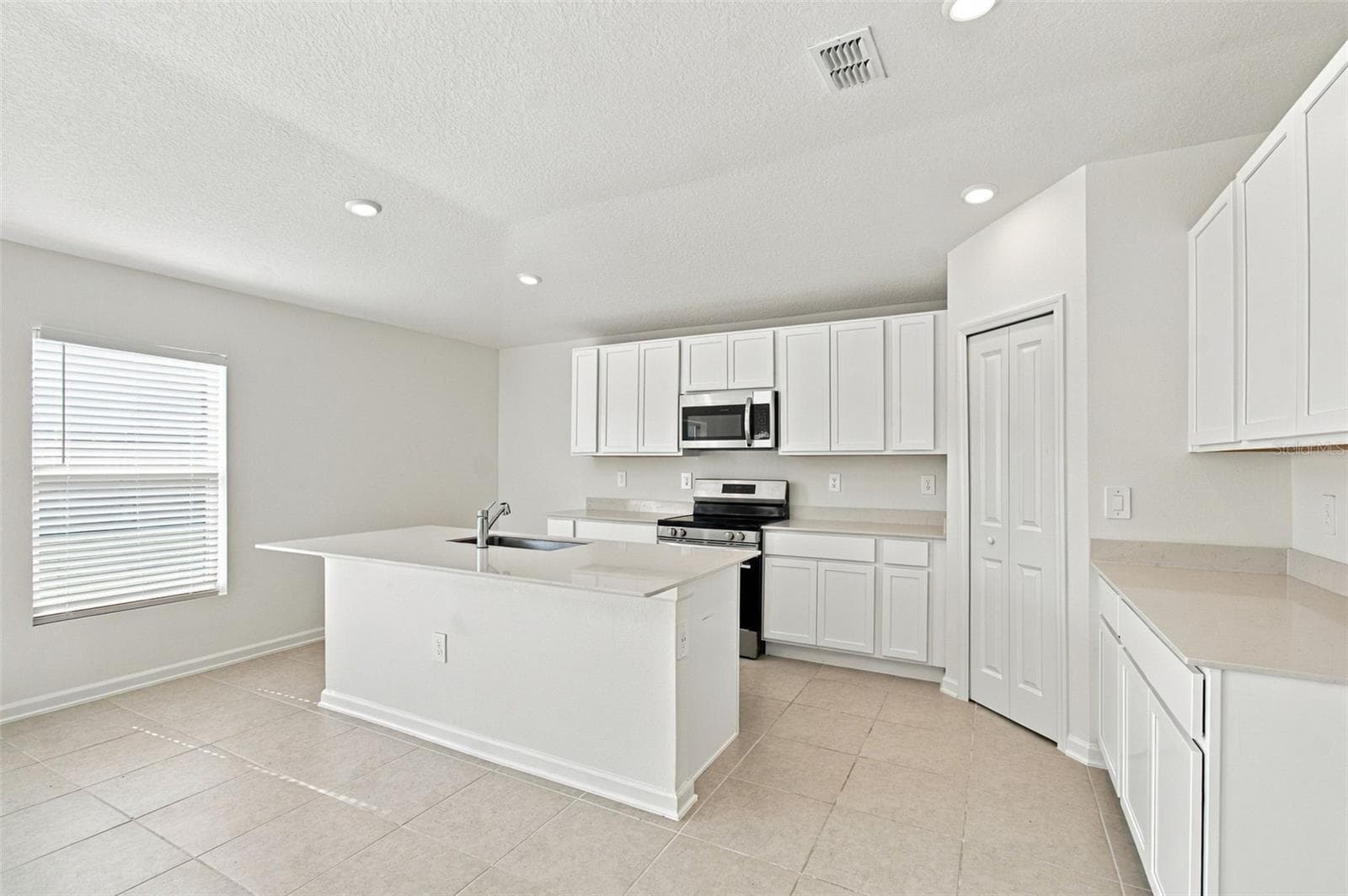 The kitchen offers a spacious island with breakfast bar, white Shaker-style cabinetry, and quartz countertops, all overlooking the dining and living areas. - 2007 FORAGE DR, KISSIMMEE
