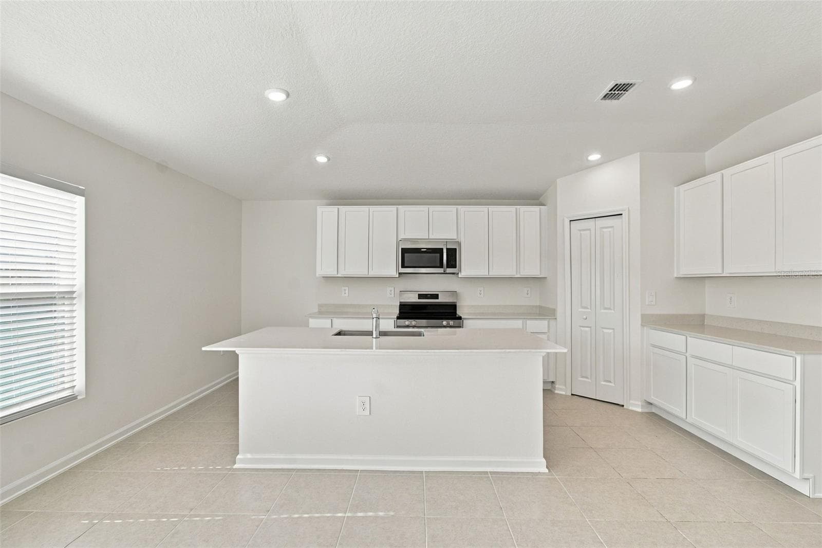 The kitchen offers a spacious island with breakfast bar, white Shaker-style cabinetry, and quartz countertops, all overlooking the dining and living areas. - 2007 FORAGE DR, KISSIMMEE