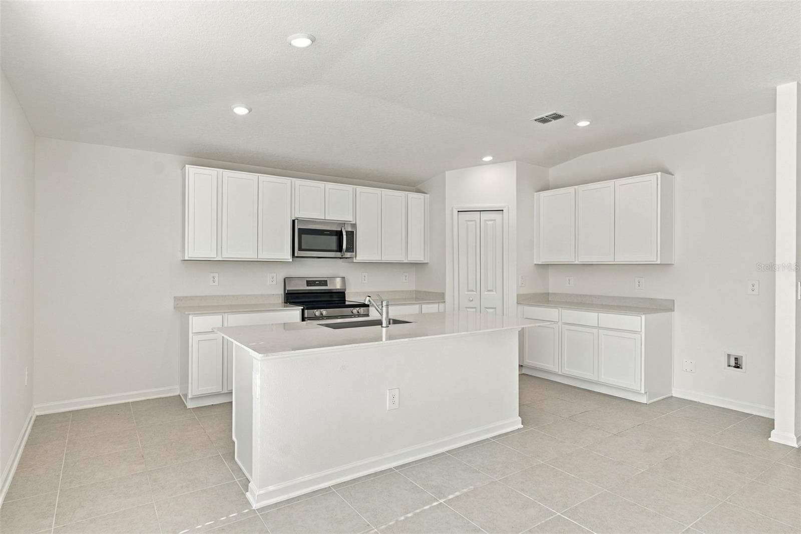 The kitchen offers a spacious island with breakfast bar, white Shaker-style cabinetry, and quartz countertops, all overlooking the dining and living areas. - 2007 FORAGE DR, KISSIMMEE
