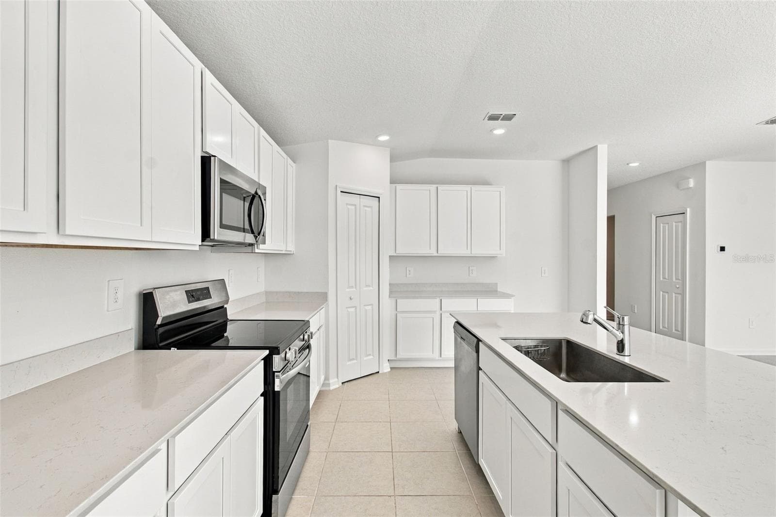 The kitchen offers a spacious island with breakfast bar, white Shaker-style cabinetry, and quartz countertops, all overlooking the dining and living areas. - 2007 FORAGE DR, KISSIMMEE