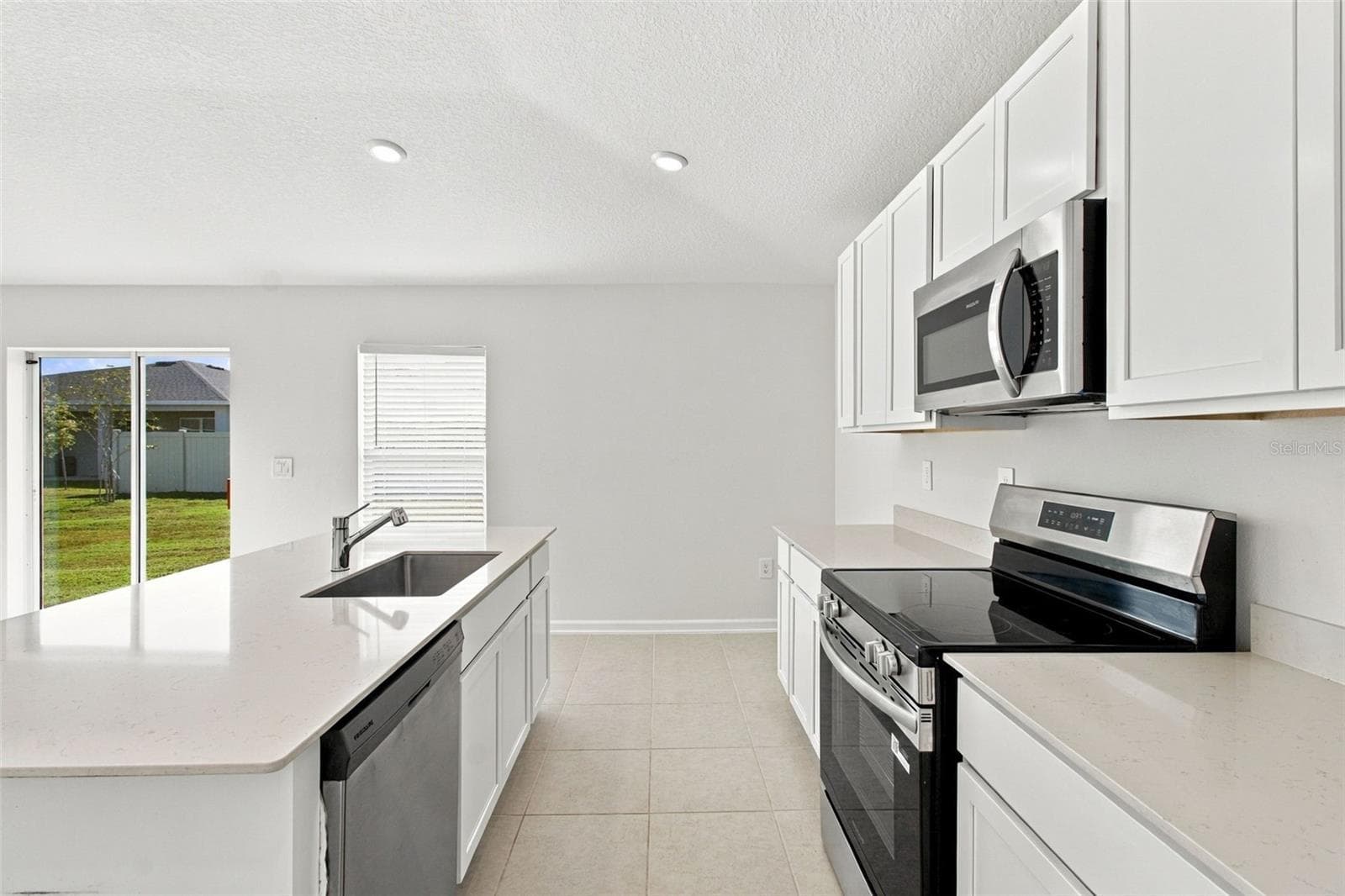 The kitchen offers a spacious island with breakfast bar, white Shaker-style cabinetry, and quartz countertops, all overlooking the dining and living areas. - 2007 FORAGE DR, KISSIMMEE