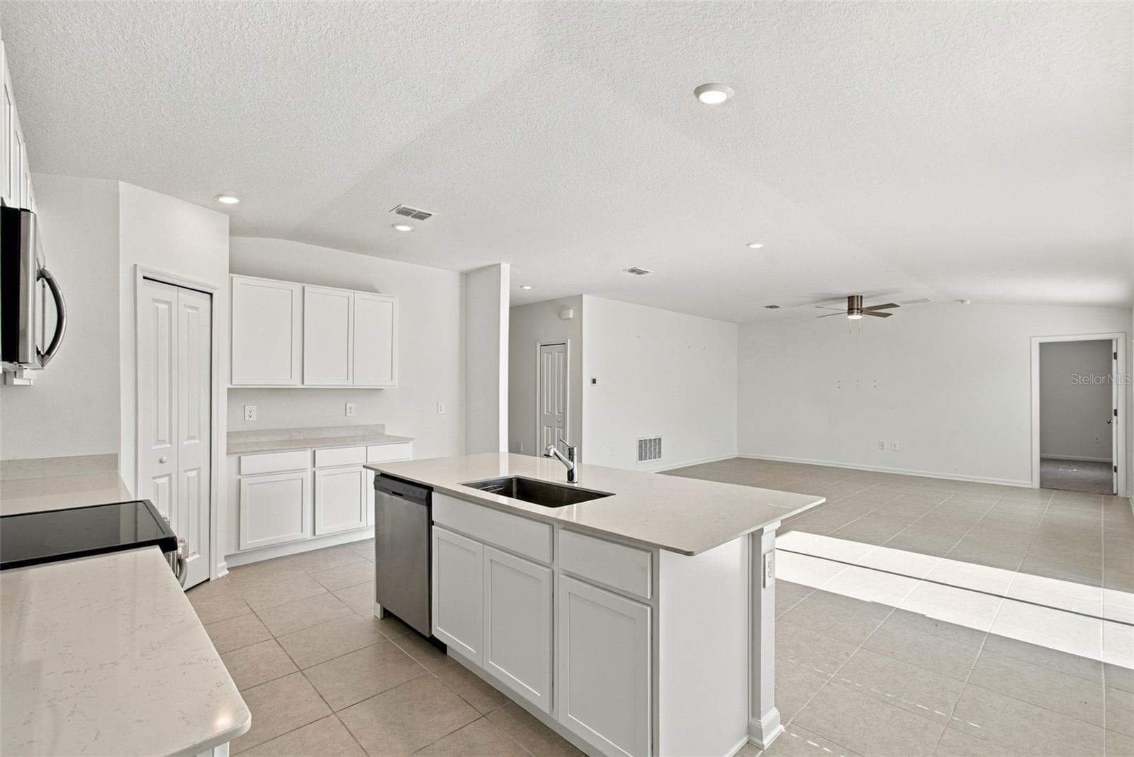 The kitchen offers a spacious island with breakfast bar, white Shaker-style cabinetry, and quartz countertops, all overlooking the dining and living areas. - 2007 FORAGE DR, KISSIMMEE