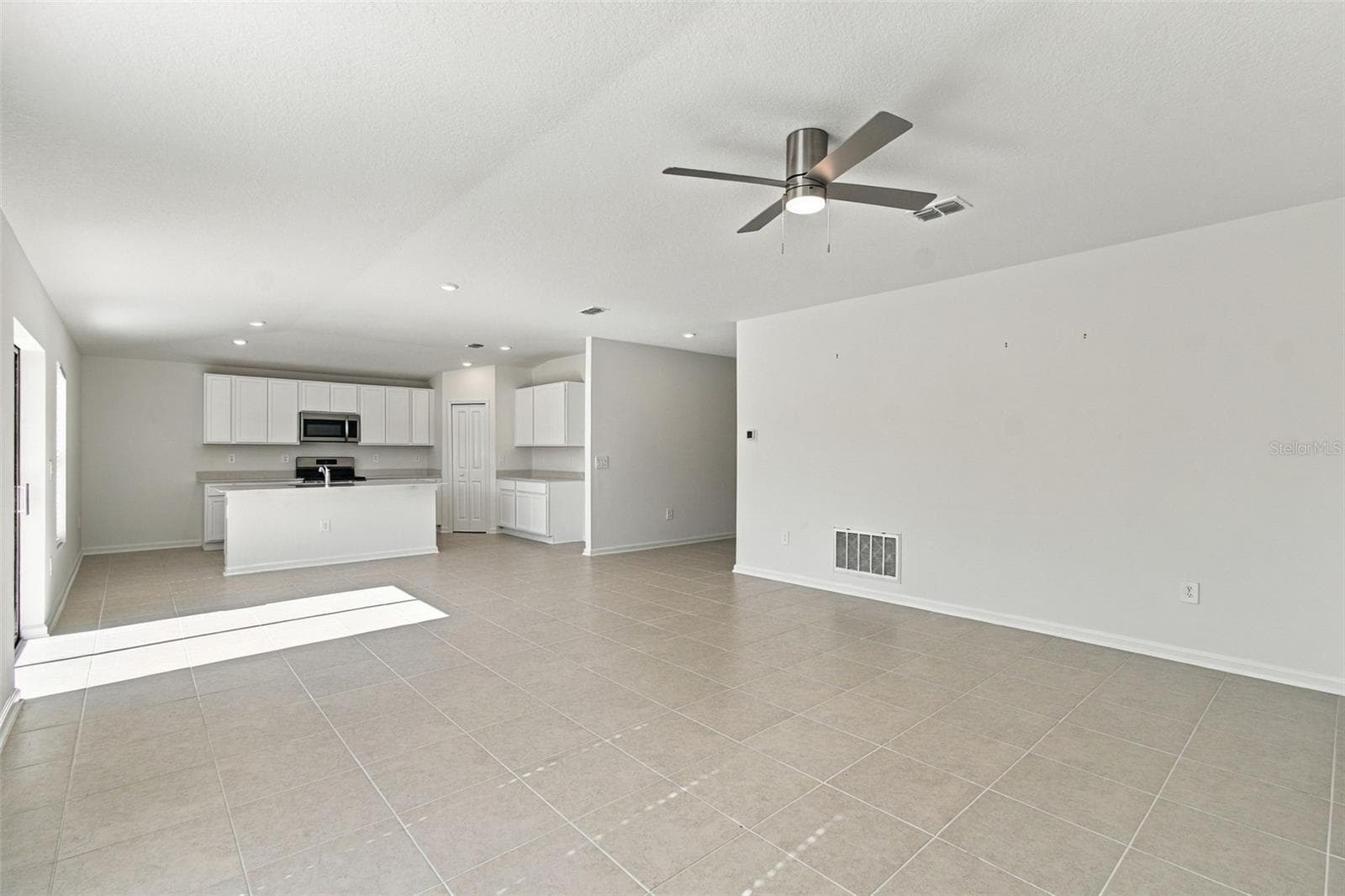 The kitchen offers a spacious island with breakfast bar, white Shaker-style cabinetry, and quartz countertops, all overlooking the dining and living areas. - 2007 FORAGE DR, KISSIMMEE