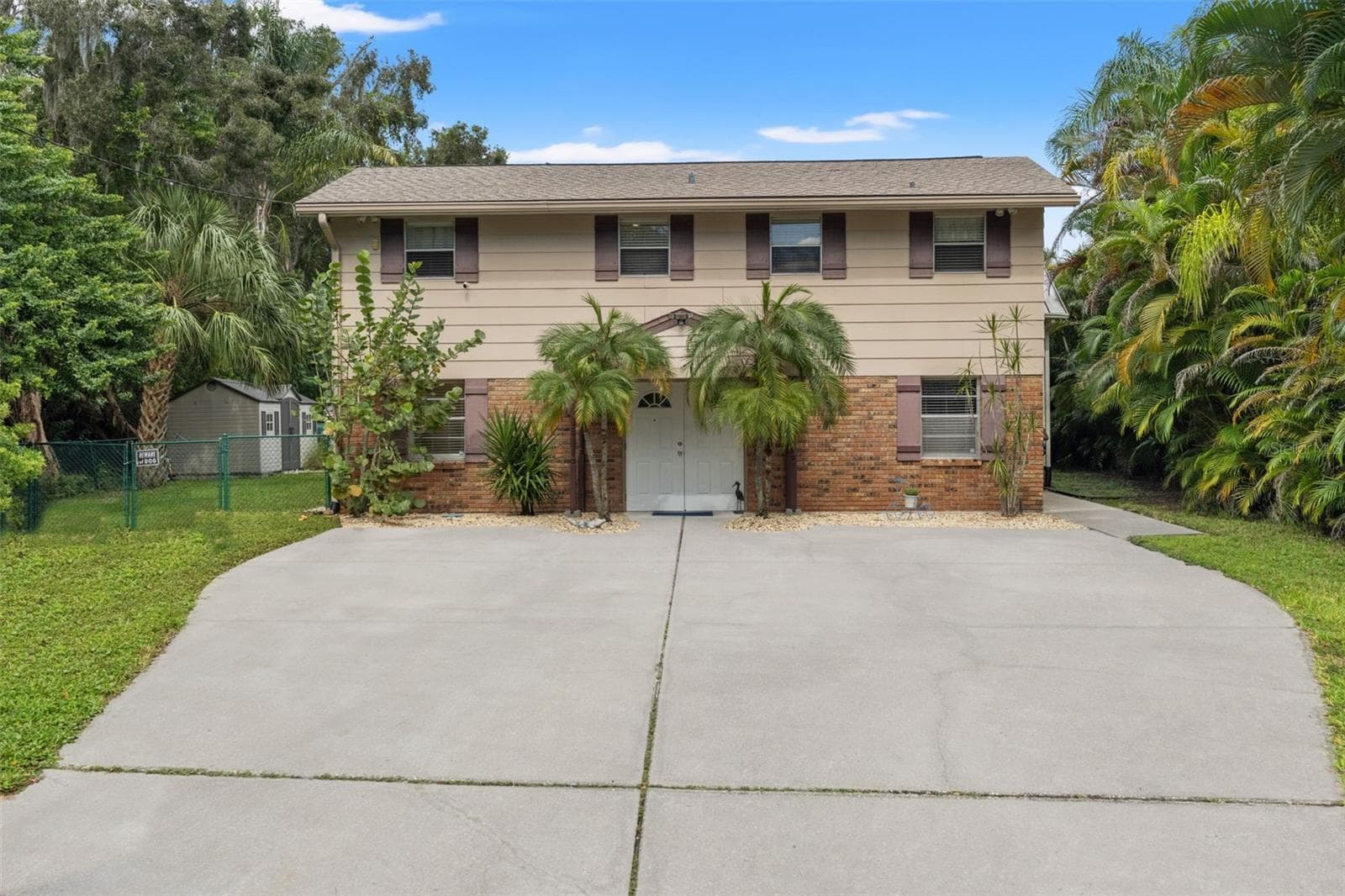 Welcome to 13 Freshwater Drive! This elevated waterfront home features a classic brick-and-siding exterior, mature tropical landscaping, and an expansive concrete driveway offering plenty of room for parking. - 13 FRESHWATER, PALM HARBOR