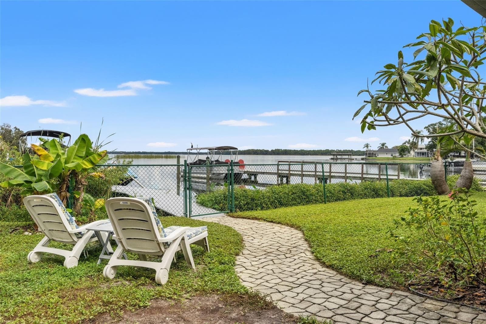 Pull up a lounge chair and enjoy the view! A paver walkway connects the backyard seating area to the waterfront gate and dock. With tropical landscaping, open water, and boats nearby, this setting captures the appeal of Florida lakefront living. - 13 FRESHWATER, PALM HARBOR
