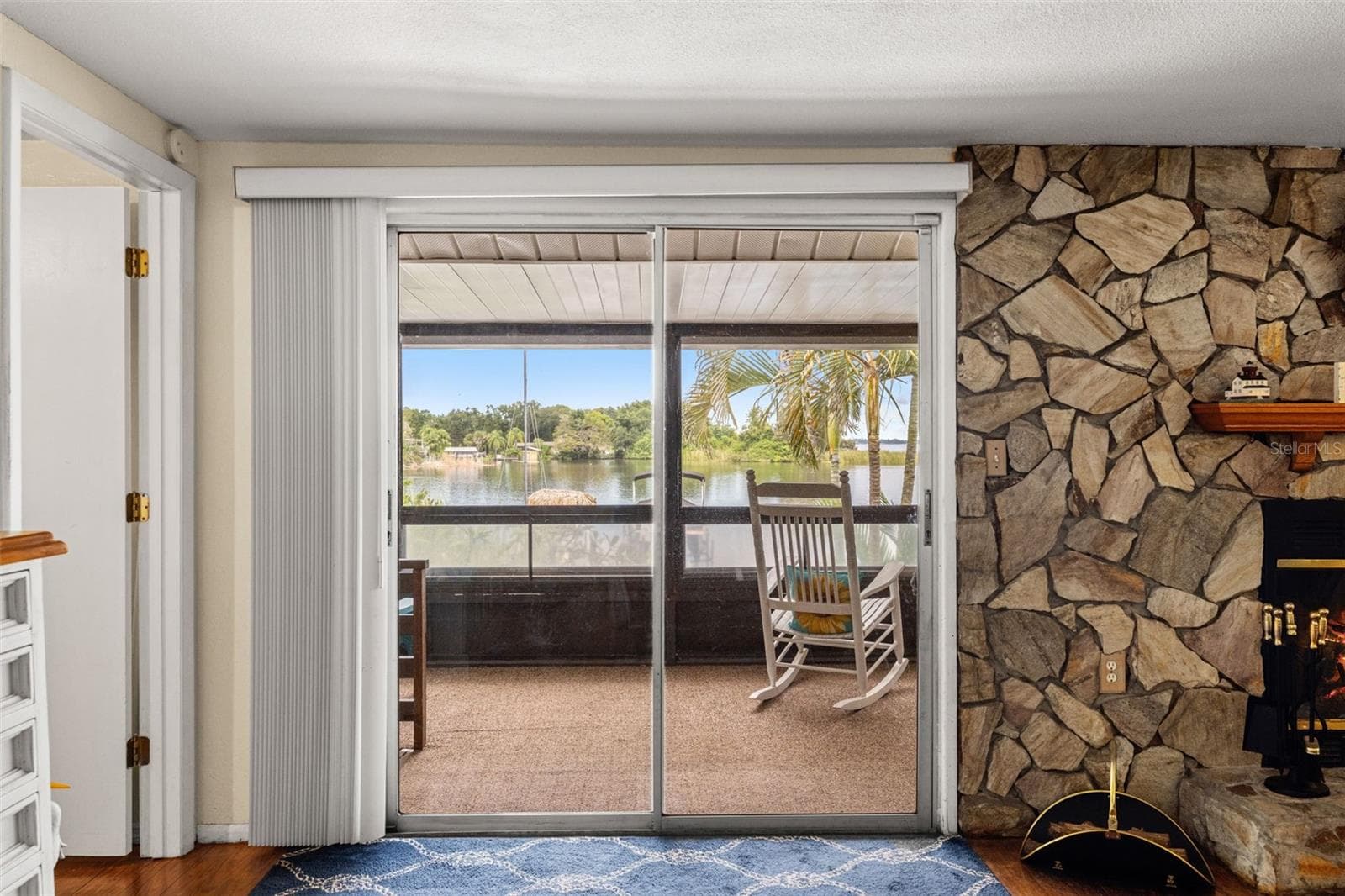 A fireplace with character! The floor-to-ceiling stone surround creates a distinctive focal point, while sliding glass doors bring in natural light and connect the living room to a screened outdoor space overlooking the water. - 13 FRESHWATER, PALM HARBOR