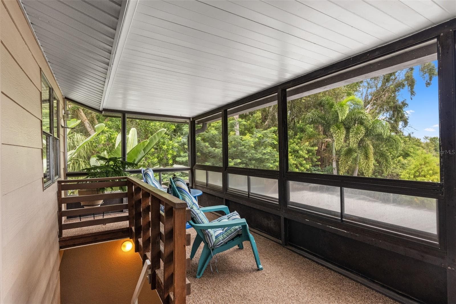 Your own peaceful escape among the palms! This elevated screened porch offers comfortable seating, lush tropical views, and a covered setting for enjoying Florida's beautiful weather. A staircase provides access to the lower level. - 13 FRESHWATER, PALM HARBOR