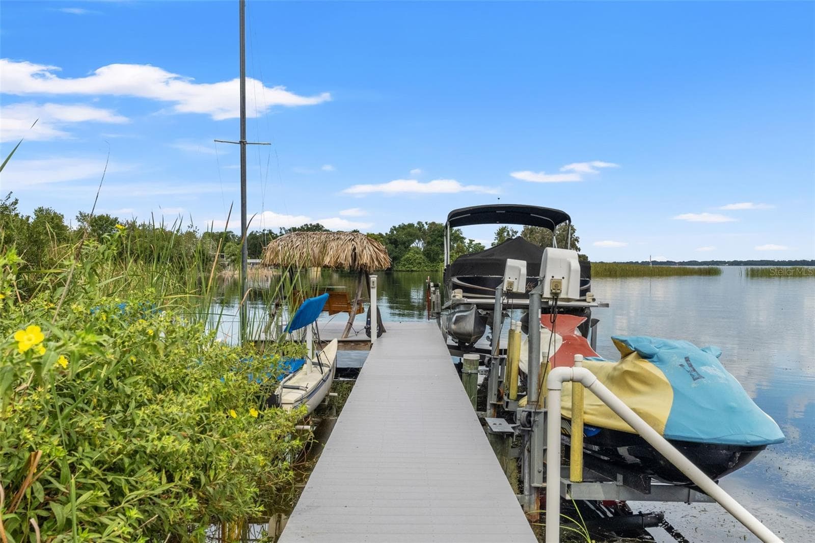 Your Florida boating lifestyle starts right here! The waterfront dock features a covered pontoon boat on a lift, personal watercraft lift, and space for additional recreational equipment. A thatched-roof seating area at the end of the dock offers a relaxing spot overlooking the lake. - 13 FRESHWATER, PALM HARBOR