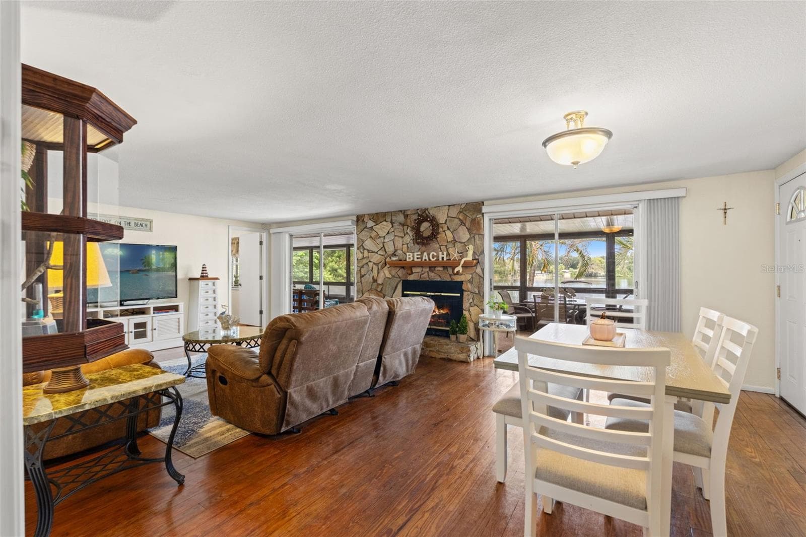 Waterfront views take center stage! The open living and dining areas feature beautiful wood flooring, a floor-to-ceiling stone fireplace, and sliding glass doors overlooking the water. Two separate screened outdoor spaces extend the living area. - 13 FRESHWATER, PALM HARBOR