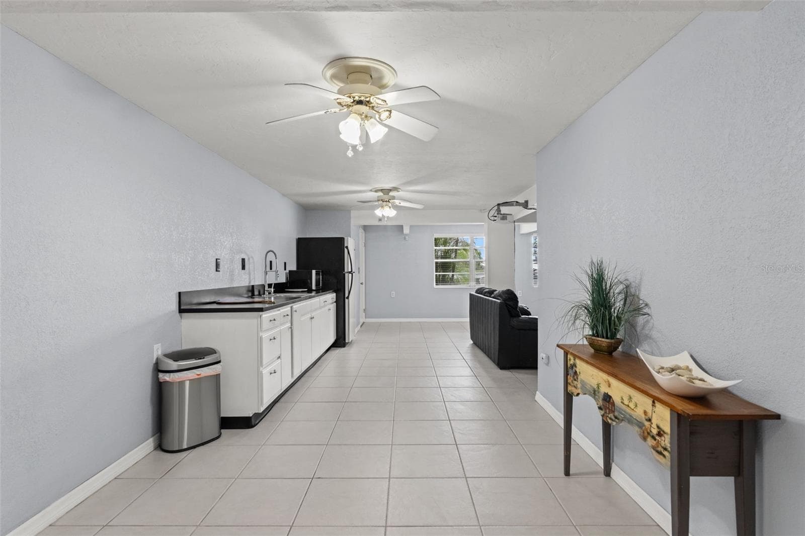 The home's lower level offers a convenient kitchenette with white cabinetry, contrasting dark countertops, a sink, refrigerator, and microwave. Neutral tile flooring extends throughout the space, connecting the kitchenette with the adjoining living area. A practical setup for entertaining, hosting guests, or enjoying additional space separate from the main living level. - 13 FRESHWATER, PALM HARBOR