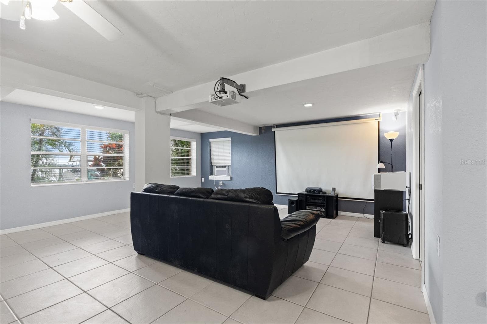 Movie nights have their own dedicated space! The lower-level living area is currently arranged as a home theater, complete with a large projection screen, ceiling-mounted projector, and comfortable seating. Multiple windows bring natural light into the room, making it equally suitable for everyday relaxation. - 13 FRESHWATER, PALM HARBOR