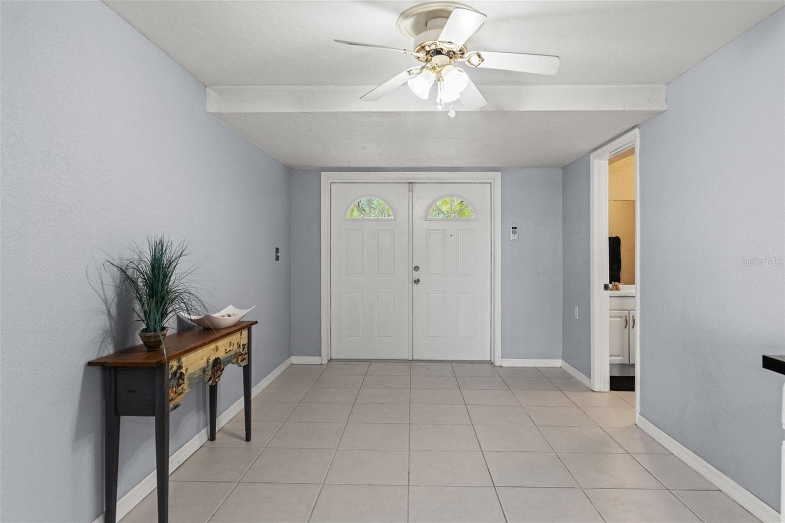 Double entry doors welcome you into the home's lower level, where neutral tile flooring, light-colored walls, and ceiling fans create a versatile space. With its own exterior entrance and nearby bathroom, this level offers flexibility for a variety of household needs. - 13 FRESHWATER, PALM HARBOR