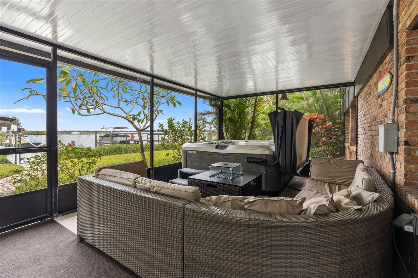 Your waterfront retreat continues downstairs! This spacious screened patio features a hot tub, comfortable sectional seating, and views toward the water. Surrounded by tropical landscaping, it's an inviting place to entertain or unwind after a day on the lake. - 13 FRESHWATER, PALM HARBOR