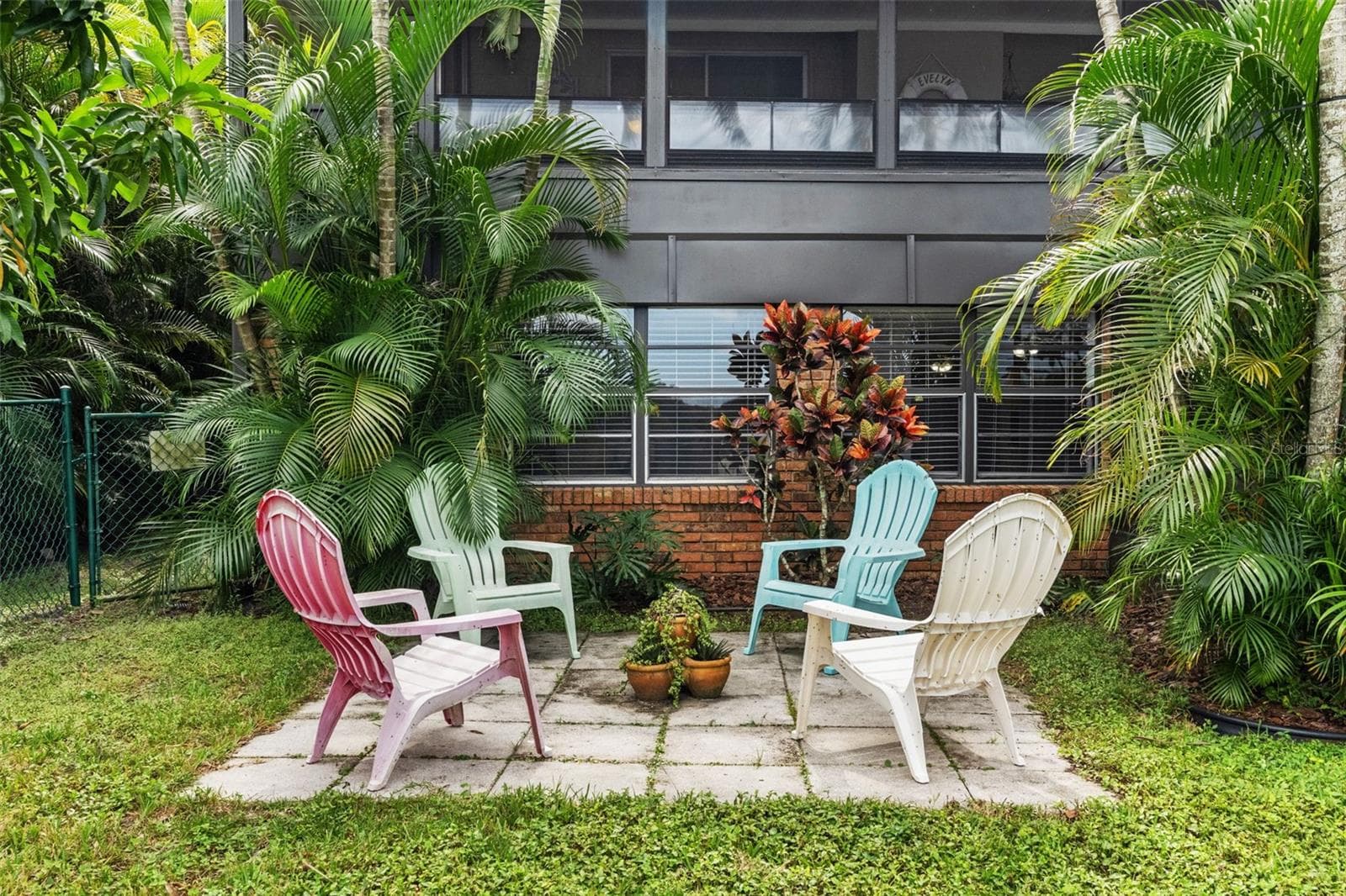 Tucked among lush palms and colorful tropical plants, this charming outdoor seating area offers another place to unwind. Four Adirondack-style chairs create a casual gathering spot beneath the home's elevated screened porch. - 13 FRESHWATER, PALM HARBOR