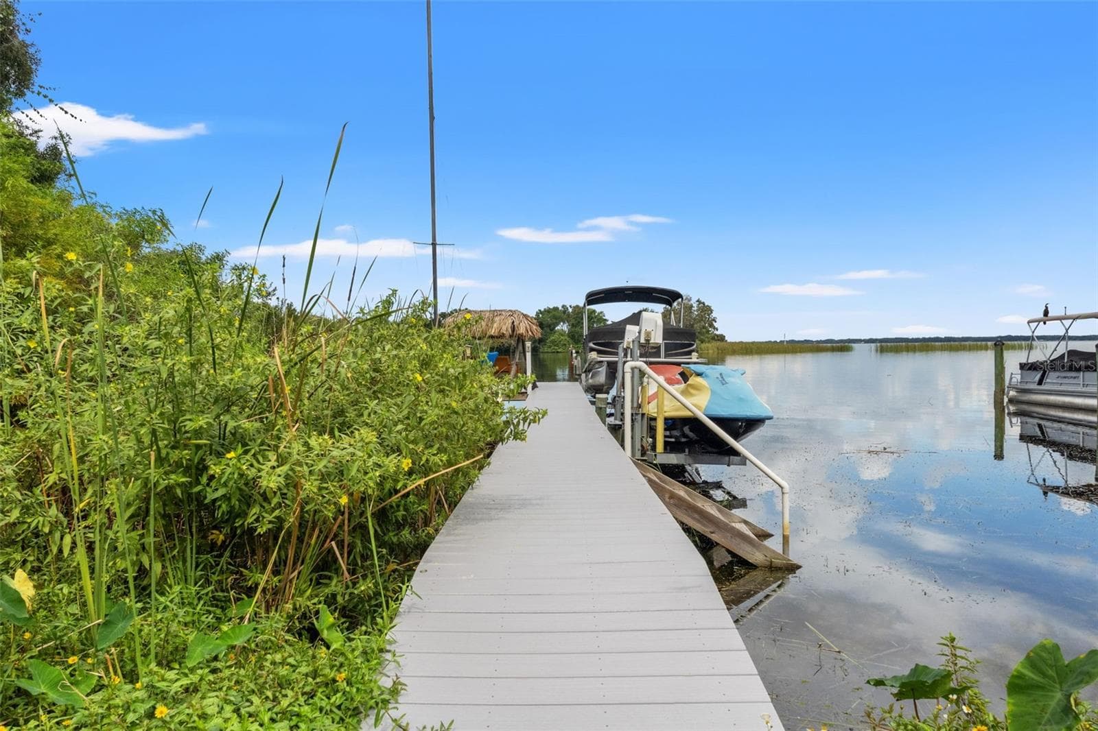 A walkway leads directly to the waterfront dock, where a boat and personal watercraft are pictured alongside the calm lake. With expansive water views stretching toward the distant shoreline, this is an inviting setting for boating, fishing, and enjoying life on the water. - 13 FRESHWATER, PALM HARBOR