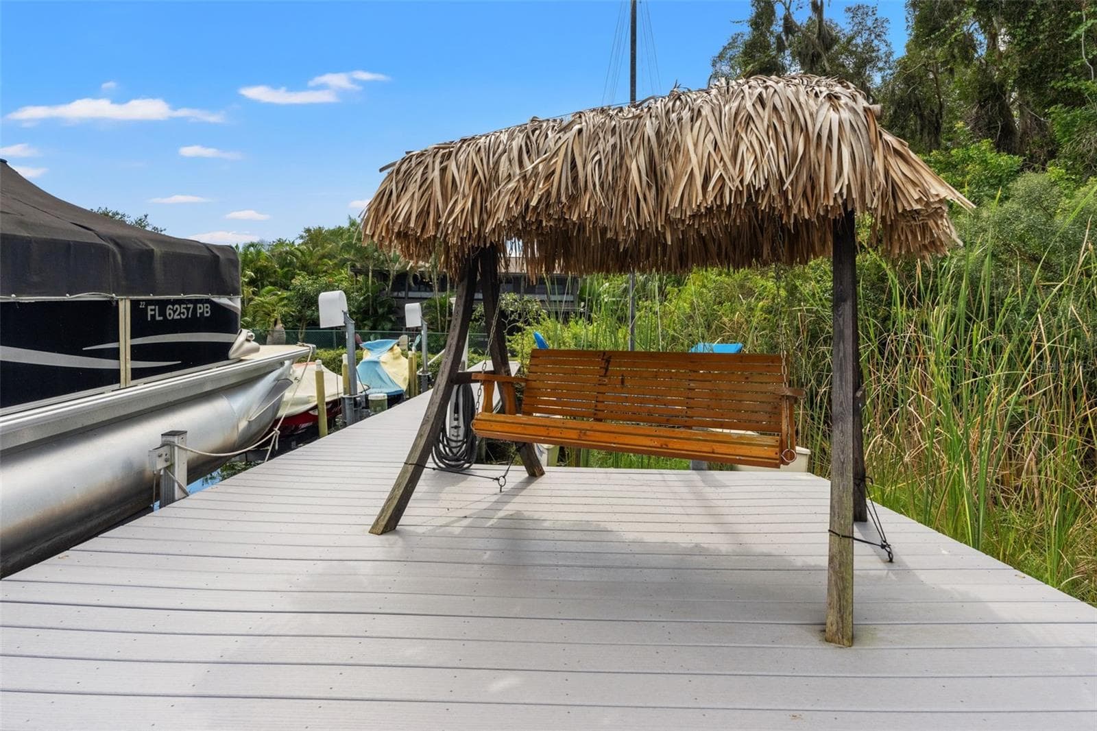 A little slice of paradise right on the water! The dock features a wooden swing beneath a tropical thatched roof, creating a shaded place to relax beside the lake. It's an inviting spot to unwind after boating or simply enjoy the waterfront atmosphere. - 13 FRESHWATER, PALM HARBOR