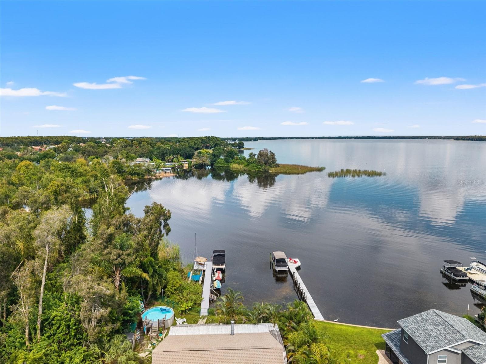 This aerial view showcases the home's waterfront location, private dock, and tropical backyard, including an above-ground pool. Mature landscaping provides a lush setting, while the lake opens into an impressive expanse of water just beyond the dock. - 13 FRESHWATER, PALM HARBOR