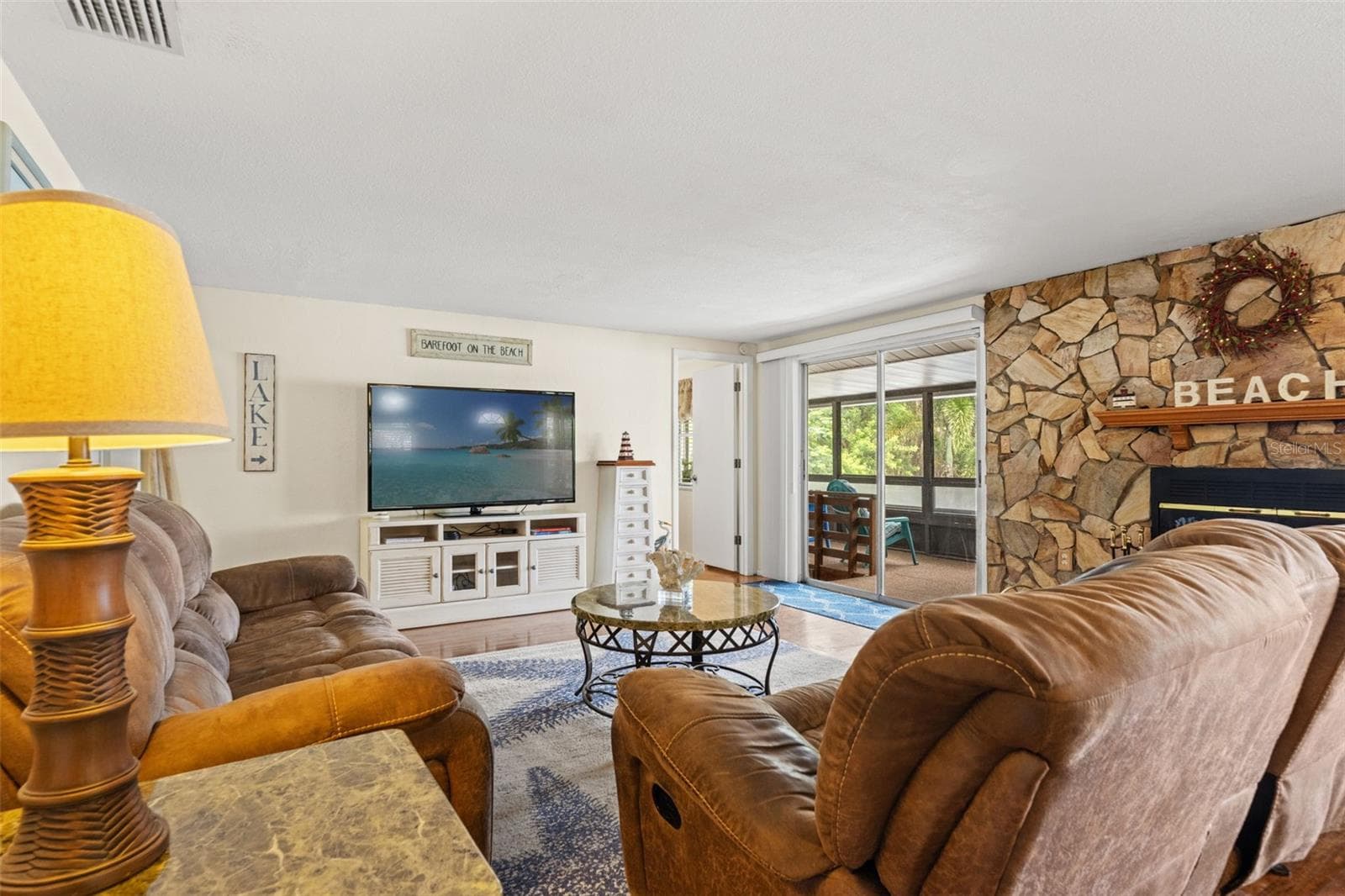 Comfortable, inviting, and full of character! The living room offers generous seating space, warm wood flooring, and direct access to a screened porch. The stone fireplace adds a cozy touch to this waterfront retreat. - 13 FRESHWATER, PALM HARBOR