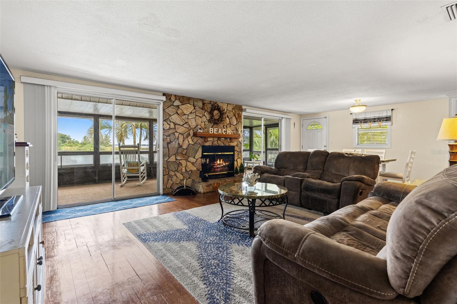 The spacious living room offers flexible furniture arrangements, wood flooring, and convenient access to the screened porch. Two nearby doorways connect to additional rooms, making the upper-level layout both practical and comfortable. - 13 FRESHWATER, PALM HARBOR