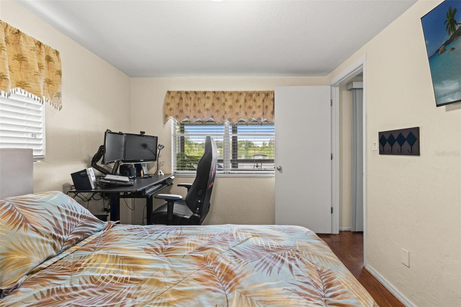 This versatile bedroom offers wood flooring, two windows for natural light, and a built-in closet. Currently arranged with both a bed and computer workstation, it demonstrates how easily the room accommodates sleeping and home office needs. - 13 FRESHWATER, PALM HARBOR