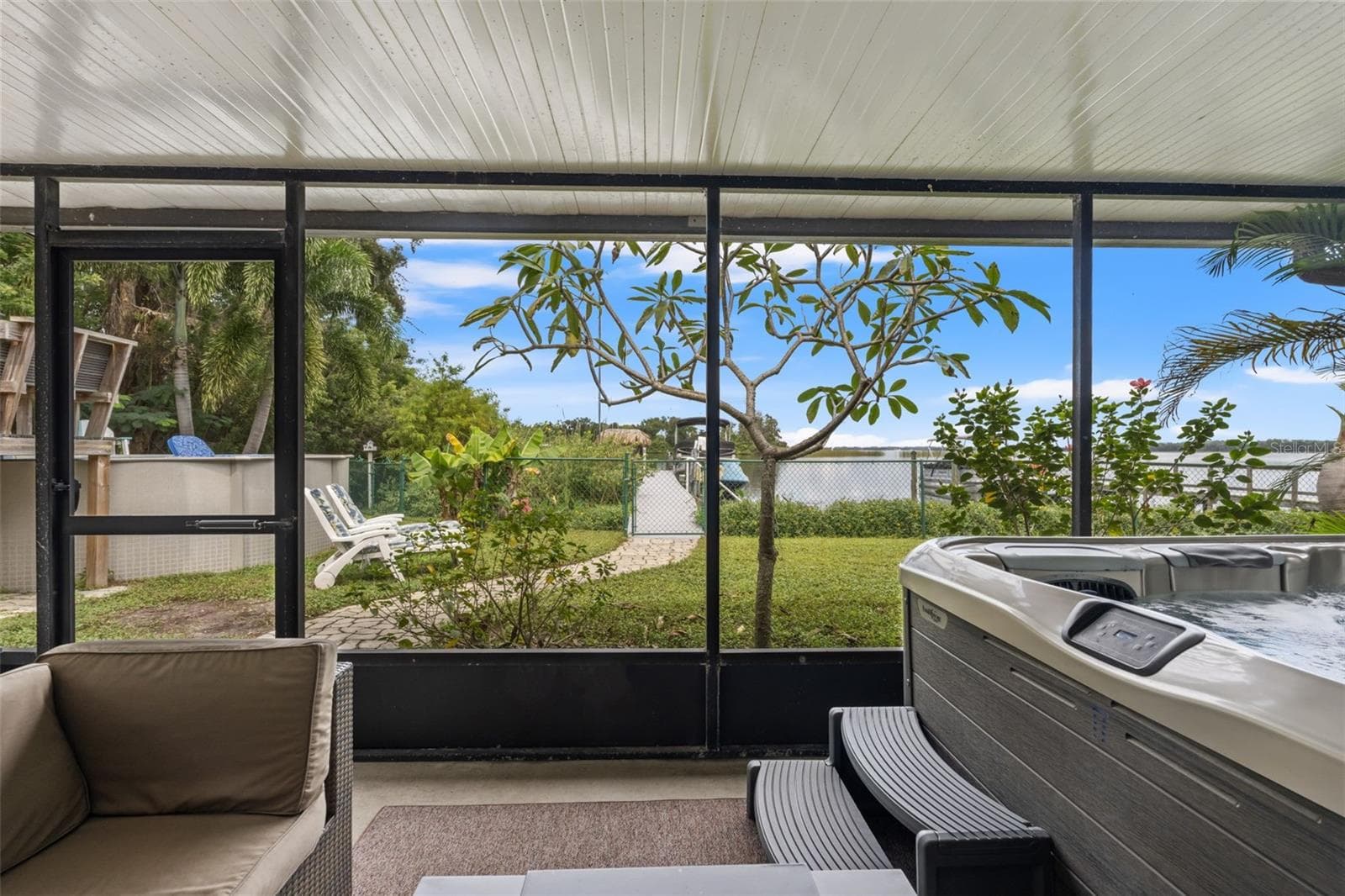 The lower-level screened patio overlooks a grassy backyard with a pathway leading toward the waterfront. Enjoy views of the dock and boats beyond, with additional outdoor recreation space just steps away. - 13 FRESHWATER, PALM HARBOR