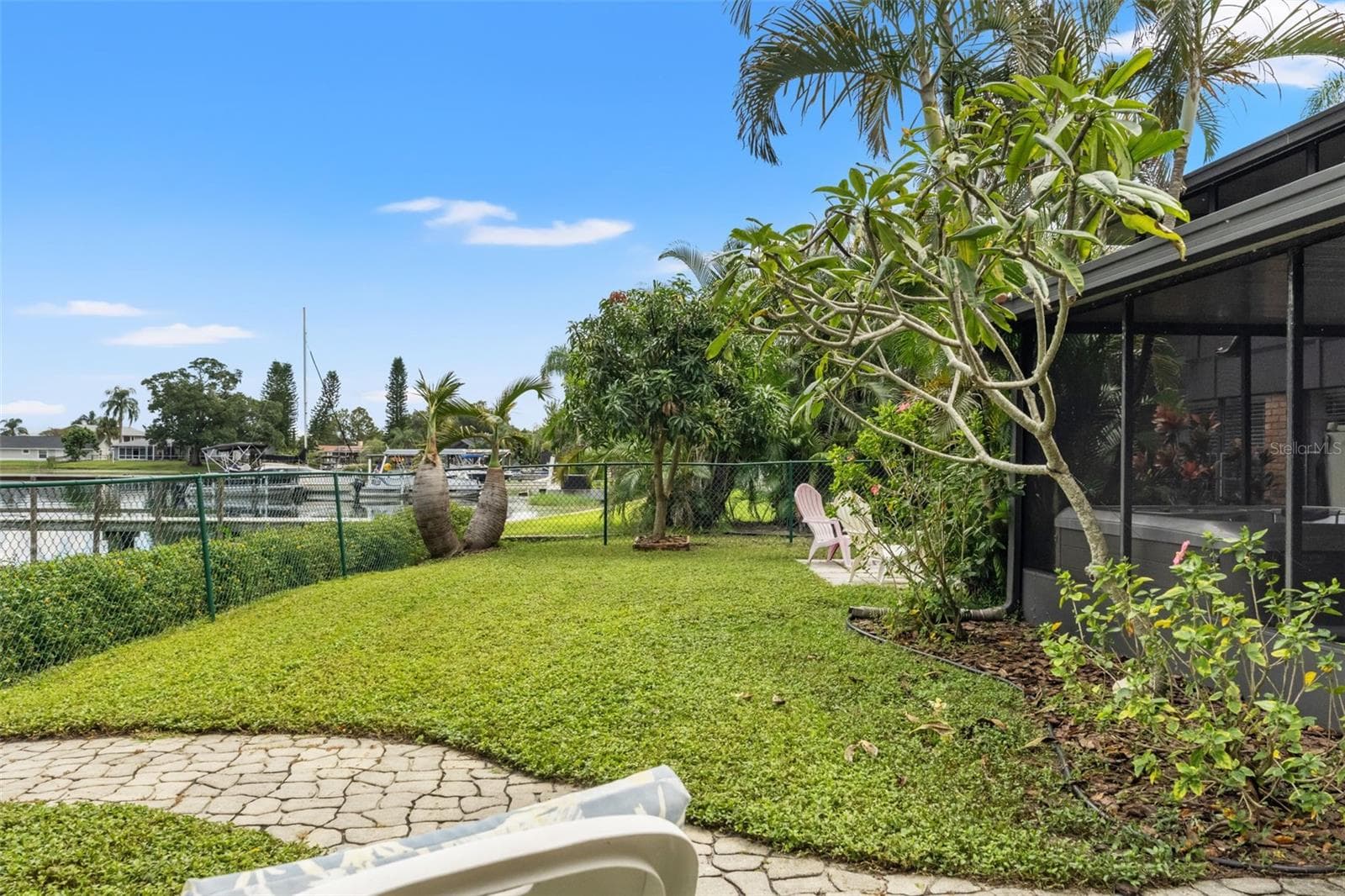 The waterfront backyard offers a lovely combination of open lawn, flowering plants, and mature tropical landscaping. With room to relax outdoors and views toward neighboring docks and boats, this setting makes the most of its lakeside location. - 13 FRESHWATER, PALM HARBOR