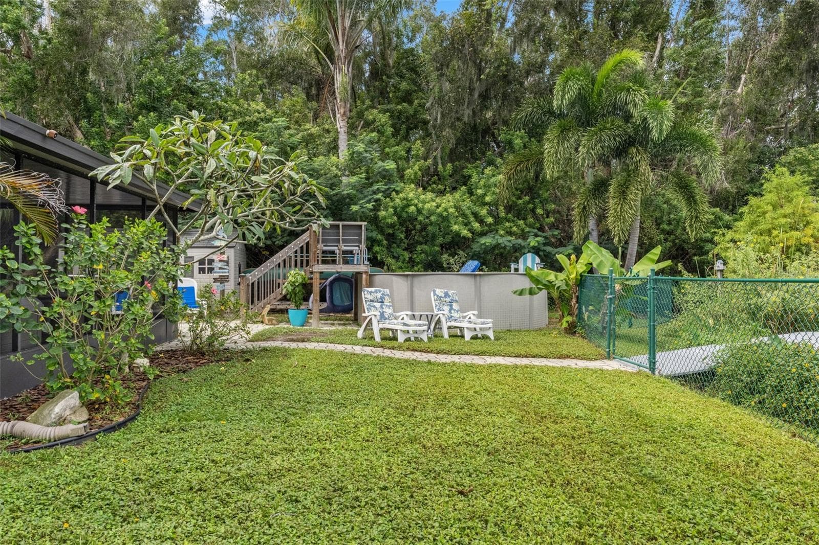 Enjoy your own backyard retreat with an above-ground pool, raised wooden deck, and surrounding lounge areas. Mature trees and tropical landscaping create a leafy backdrop, while the nearby lawn and paver walkway provide space to enjoy the outdoors. - 13 FRESHWATER, PALM HARBOR