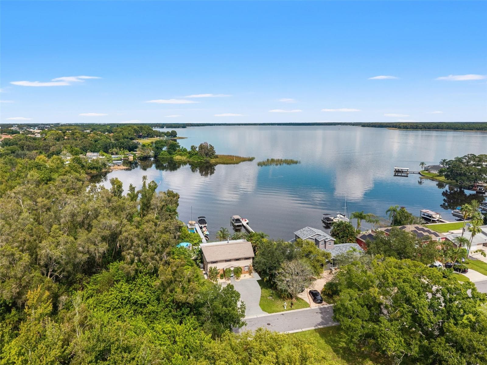 This aerial view captures the home's waterfront setting, with a private dock extending into the lake and mature trees surrounding the property. The natural shoreline, neighboring docks, and wide-open water create a beautiful backdrop for Florida lakefront living. - 13 FRESHWATER, PALM HARBOR