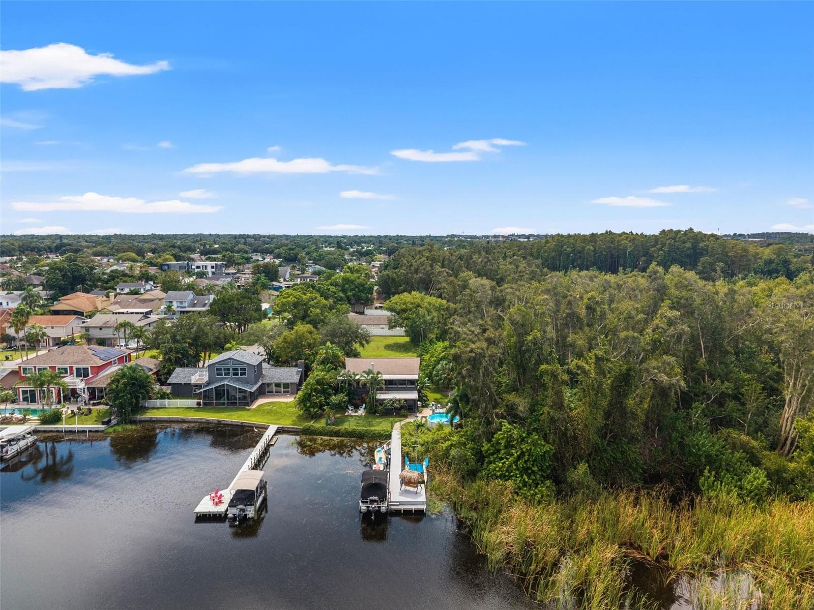 Aerial photography highlights the property's setting alongside a heavily wooded natural area, with neighboring waterfront homes and private docks lining the shoreline. The combination of mature trees, tropical landscaping, and water access creates an appealing Florida lifestyle. - 13 FRESHWATER, PALM HARBOR