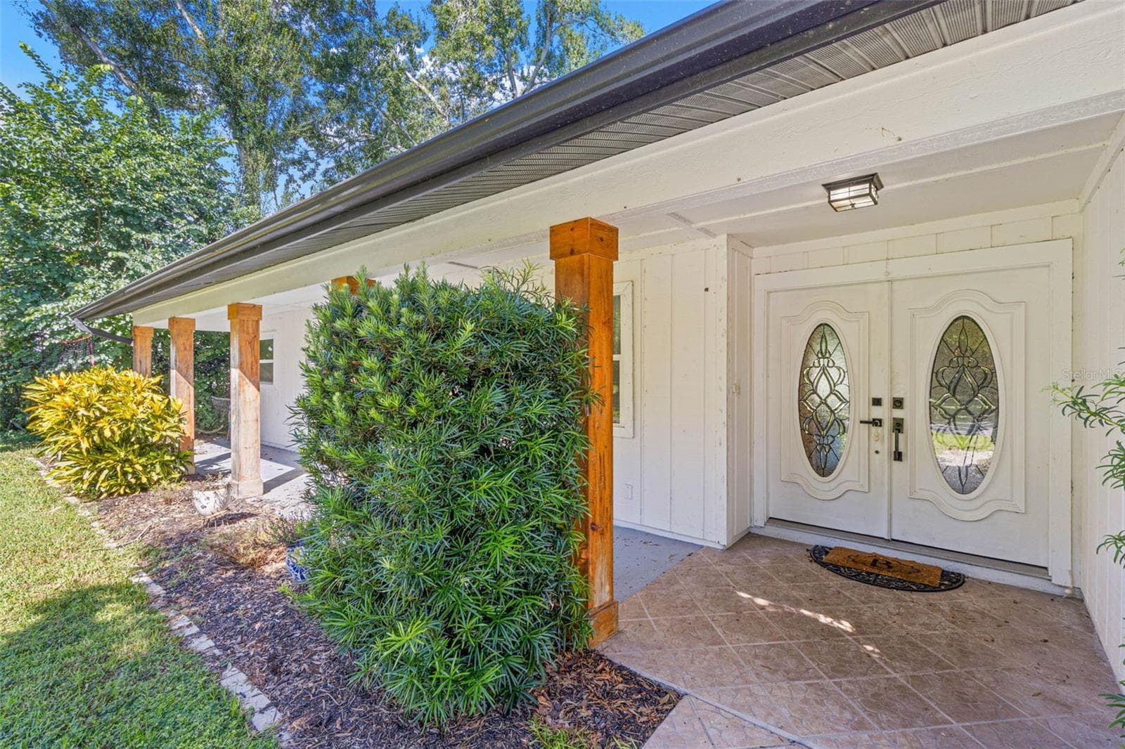A closer look at the inviting covered front porch, featuring tiled flooring, natural wood columns, decorative double entry doors with oval glass inserts, and thoughtfully placed landscaping. - 3013 GRAHAM LN, TAMPA