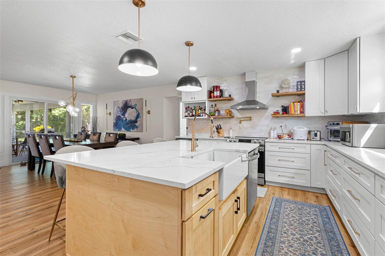 A chef-inspired kitchen with an apron-front farmhouse sink, professional-style gold faucet, convenient pot filler above the range, stainless steel range hood, and floating wood shelves. The oversized island provides additional cabinetry and generous workspace, while the open layout connects effortlessly to the dining area. - 3013 GRAHAM LN, TAMPA