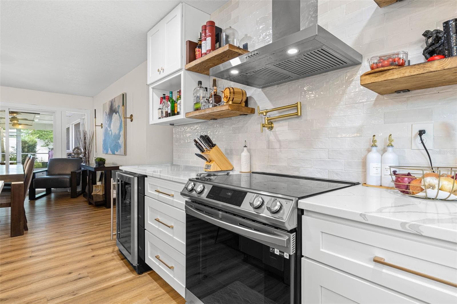 A closer look at the kitchen's stylish cooking area reveals a stainless steel smooth-top range, contemporary vent hood, convenient gold pot filler, textured subway tile backsplash, and floating wood shelves. Quartz countertops and white shaker cabinetry with gold hardware complete this beautifully coordinated space. - 3013 GRAHAM LN, TAMPA