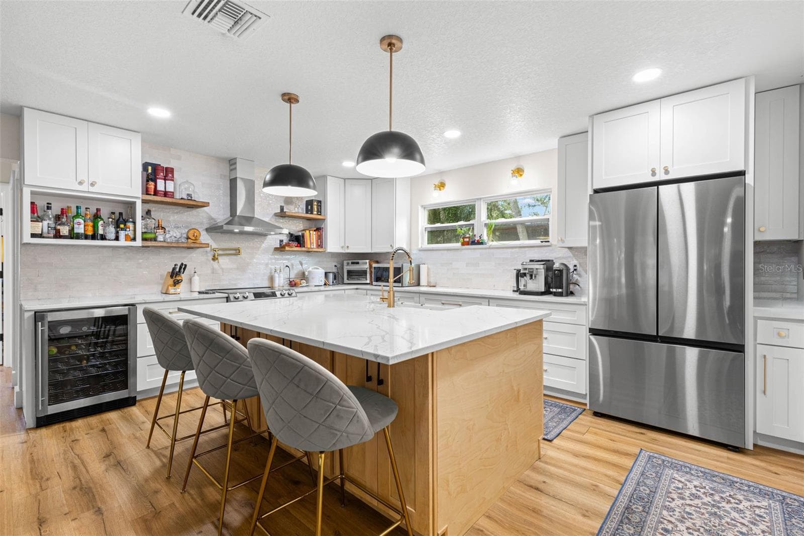 This beautifully designed kitchen combines style and practicality with abundant white shaker cabinetry, quartz countertops, stainless steel appliances, a built-in beverage refrigerator, and a generously sized center island. Floating wood shelves, gold accents, and contemporary pendant lighting add character and warmth. - 3013 GRAHAM LN, TAMPA
