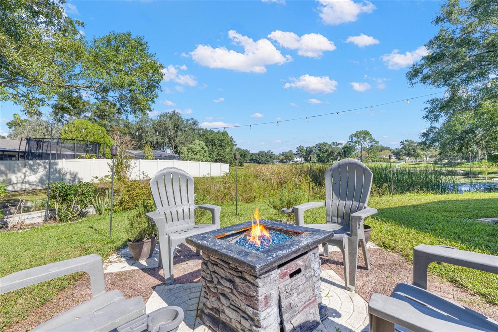 Imagine relaxing evenings under the stars in this inviting backyard retreat! A stone-look fire pit anchors the outdoor gathering area, while overhead string lighting and a peaceful pond backdrop create a charming setting for entertaining. - 3013 GRAHAM LN, TAMPA
