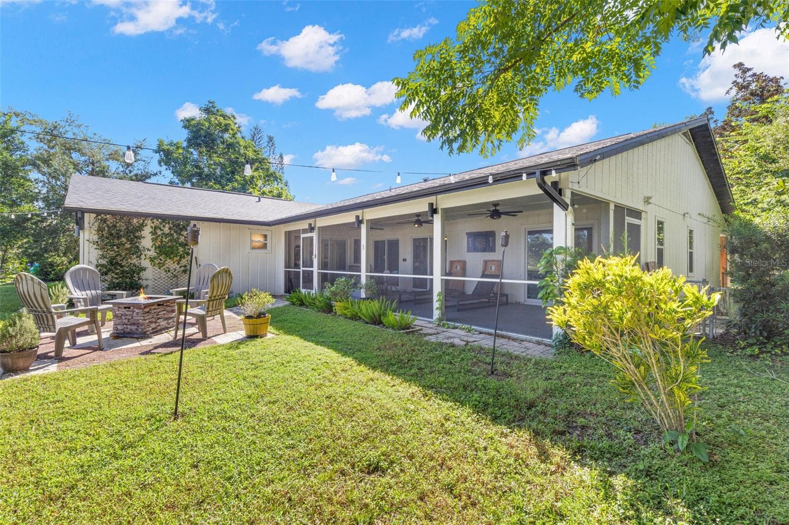 The beautifully landscaped backyard offers multiple opportunities for outdoor enjoyment, from the expansive screened porch to the open-air patio and fire pit area. Mature trees, colorful plantings, and overhead string lighting create an inviting setting for relaxing or entertaining. - 3013 GRAHAM LN, TAMPA